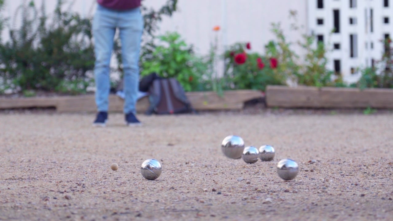 Ripresa al rallentatore di un giocatore che lancia una boccia da pétanque, colpendo un'altra boccia lontano dal boccino, il suo linguaggio del corpo mostra chiara delusione