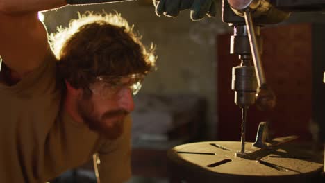 herrero caucásico con gafas de seguridad forjando herramientas metálicas en el taller