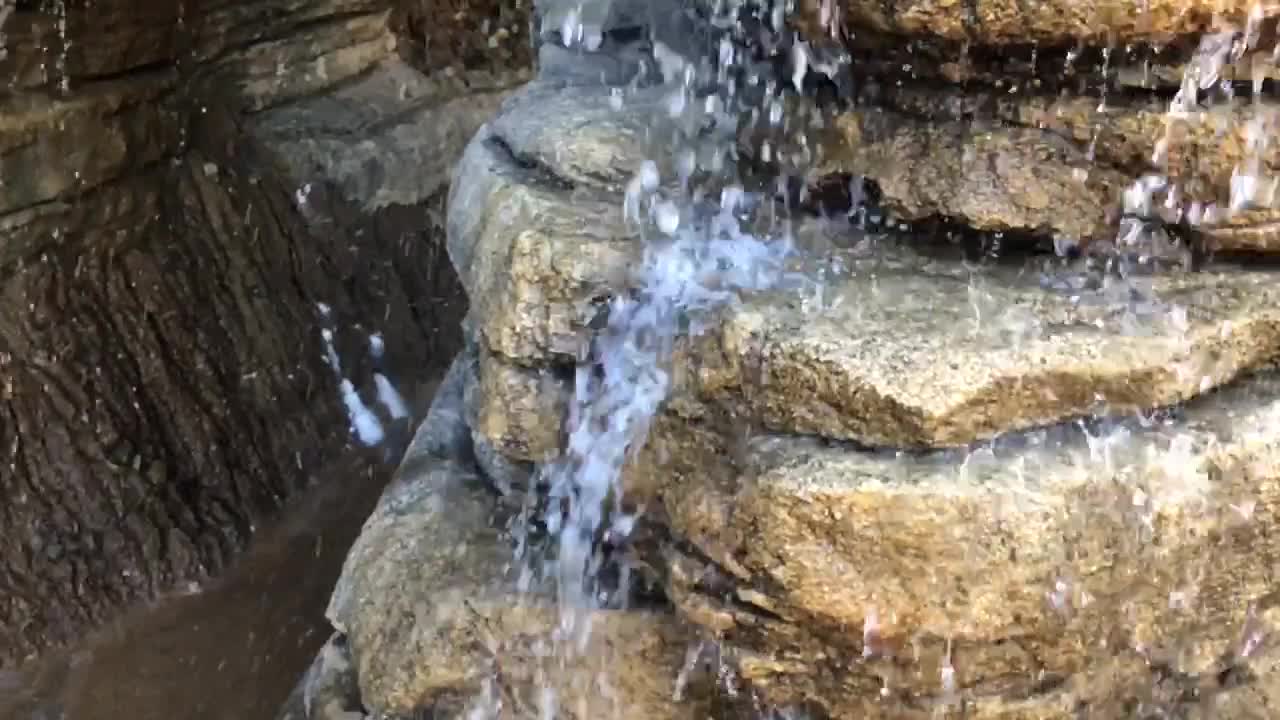 Slow motion footage of water droplets, running water, trickles, splashes, drops, and waterfalls surrounded by rock and other hard earthen material