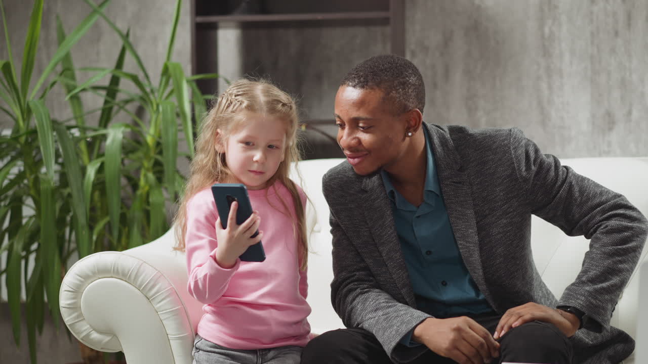 Bambina mostra i cartoni animati preferiti tramite telefono a un uomo di colore.