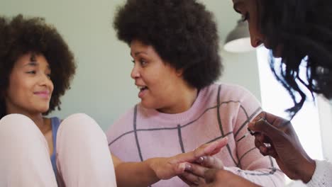 Happy-diverse-female-friends-painting-nails-and-smiling-in-bedroom