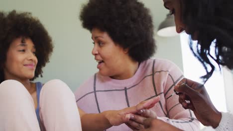 happy diverse female friends painting nails and smiling in bedroom
