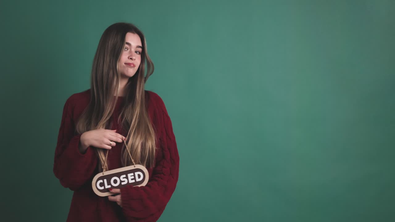 Disappointed girl standing and showing closed signboard in hand on green background