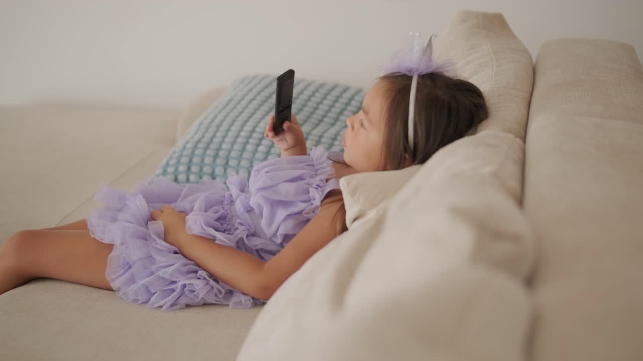 드레스를 입은 작은 소녀가 거실의 소파에서 tv를 보고 있습니다.