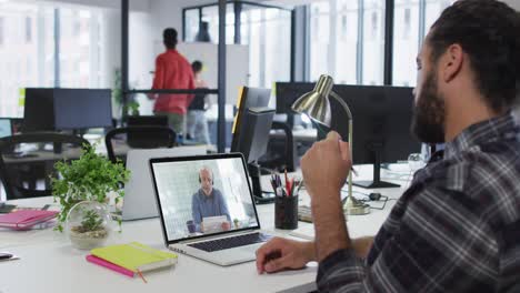 Middle-eastern-man-talking-on-video-call-with-male-office-colleague-on-laptop-at-office