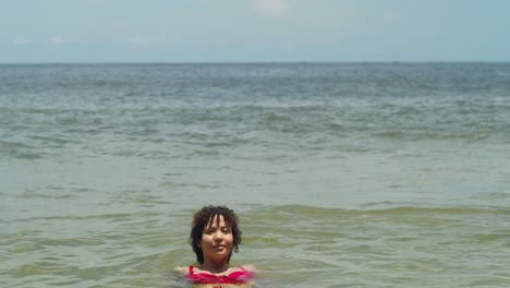 En-Un-Sensual-Bikini,-Una-Latina-De-Cabello-Rizado-Disfruta-De-La-Serenidad-De-Un-Ambiente-De-Playa-Tropical.