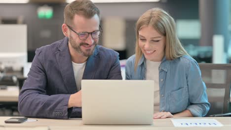 middle aged man and young woman doing high five while using laptop