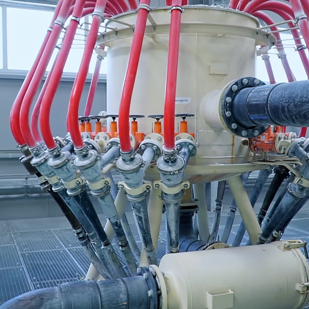 Big cistern with numerous tubes and valves attached to it and one thick bent pipe. Spacious premise with automated equipment