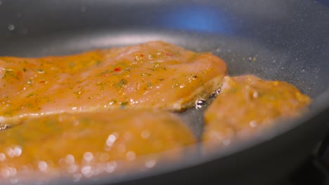 panning shot across chinese style seasoning on chicken steak fillets cooking gently in frying pan with oil bubbling underneath. food photography footage 4k.