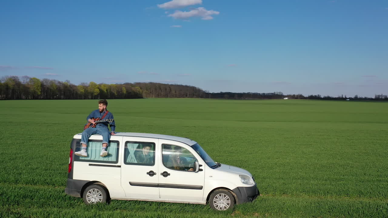 Man playing guitar on car. Young man sitting on car and playing guitar