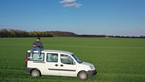 man playing guitar on car. young man sitting on car and playing guitar