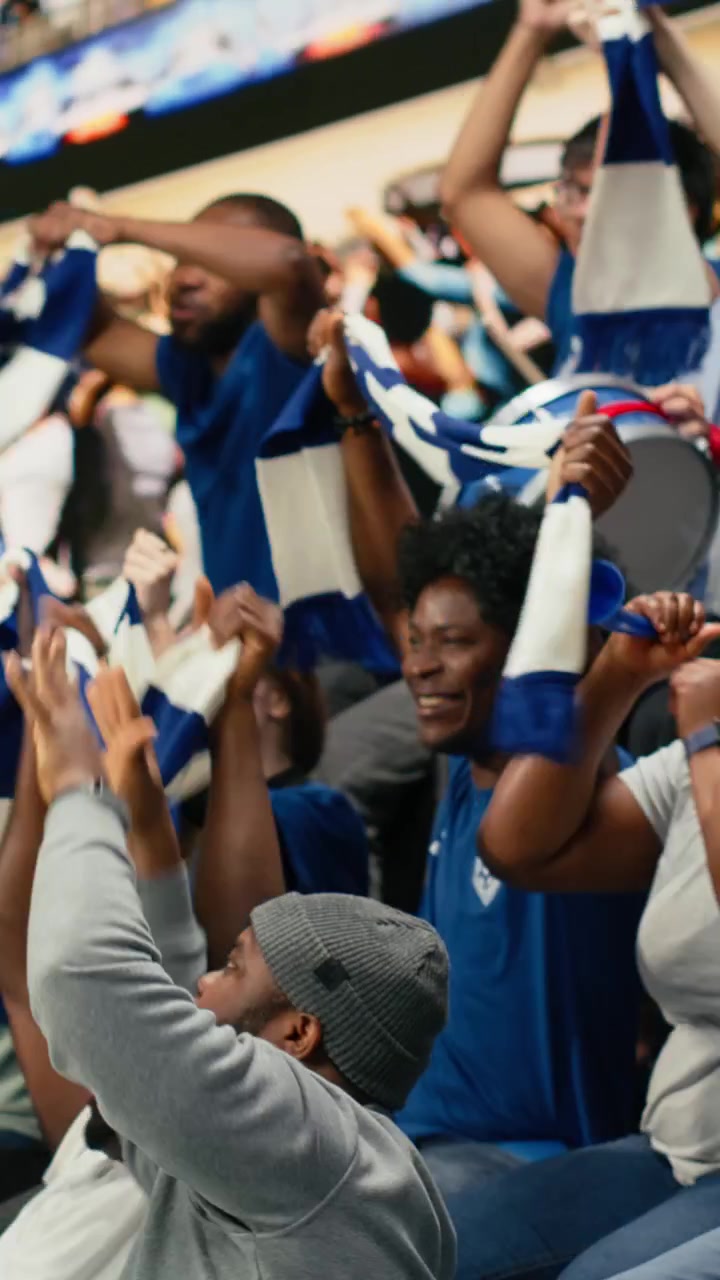 Video vertical: Capo de fútbol del equipo azul de pie sobre la multitud con un megáfono.