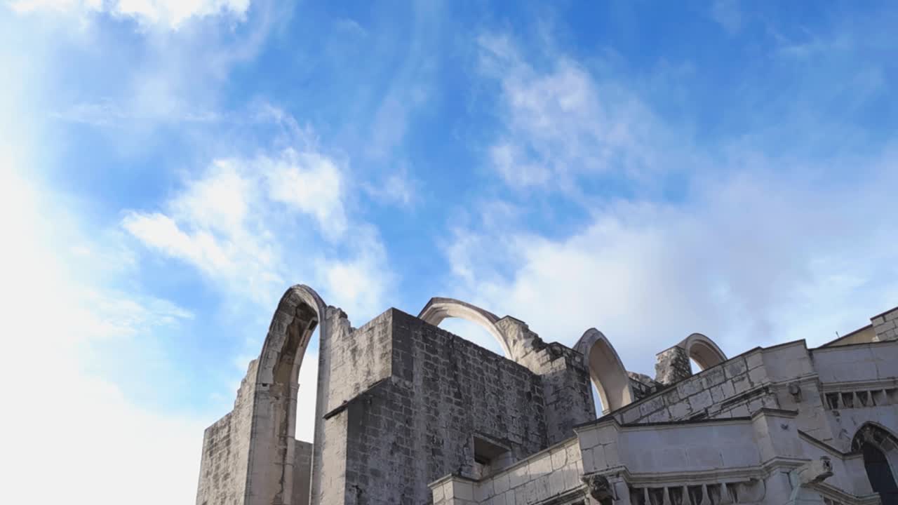 Vista ascendente panorâmica de arcos de pedra históricos e ruínas sem teto no Museu Arqueológico do Carmo, emoldurados por céu azul e nuvens macias em um dia ensolarado