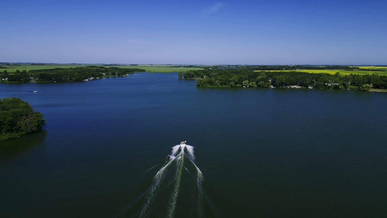 un avión no tripulado sigue a un barco de velocidad familiar que arrastra a dos wakeboarders en el lago killarney en turtle mountain, suroeste de manitoba, canadá.