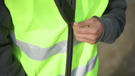 close-up of neon green reflective safety vest with black zipper partially open, showing high-visibility fluorescent fabric and horizontal silver reflective stripe, designed for outdoor worker safety