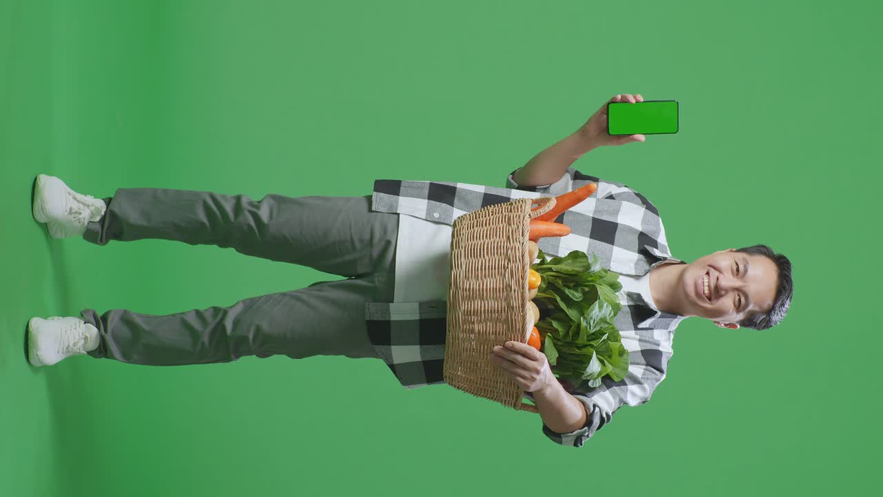 hombre sosteniendo una canasta de verduras con un teléfono inteligente
