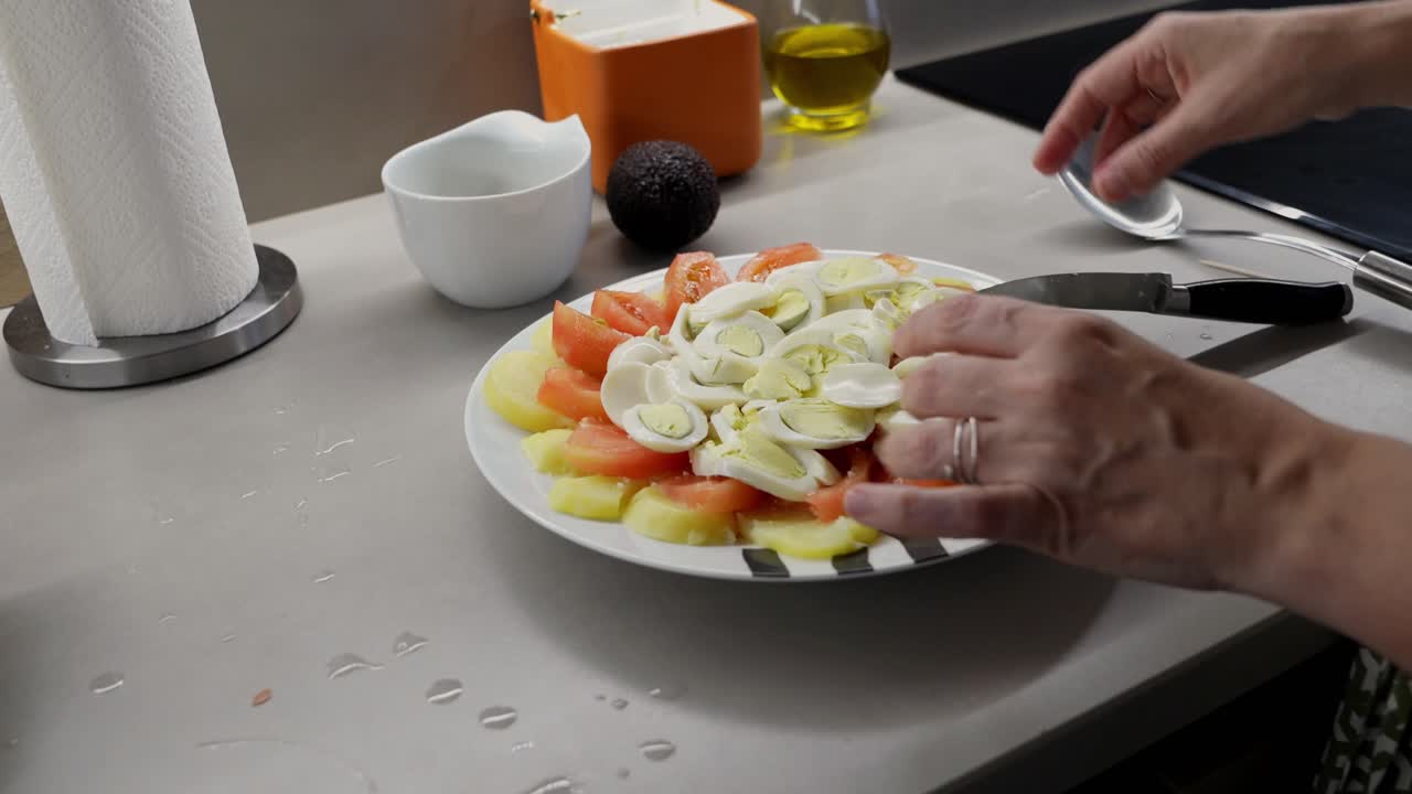 Mãos temperando uma salada fresca com batatas, tomates e ovos