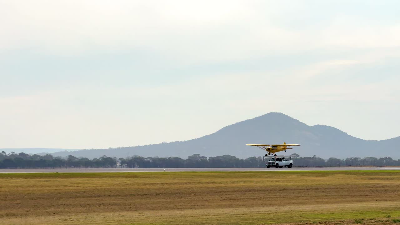 A Piper J3C-65 aircraft takes off against a scenic mountain backdrop at the Avalon Airshow in Geelong, Australia