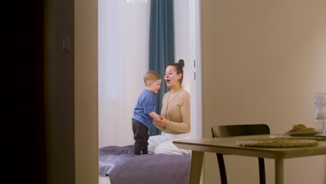 madre feliz jugando con su niño pequeño en la cama en casa 1