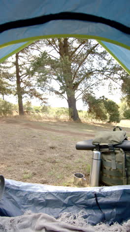 vertical video: view from tent, backpack with thermos and camping gear in forest clearing