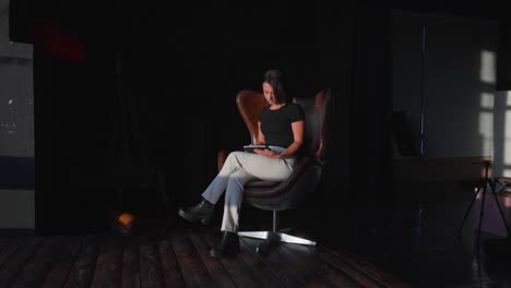 Woman-sit-on-vintage-aviator-leather-egg-chair-with-tablet-in-hands