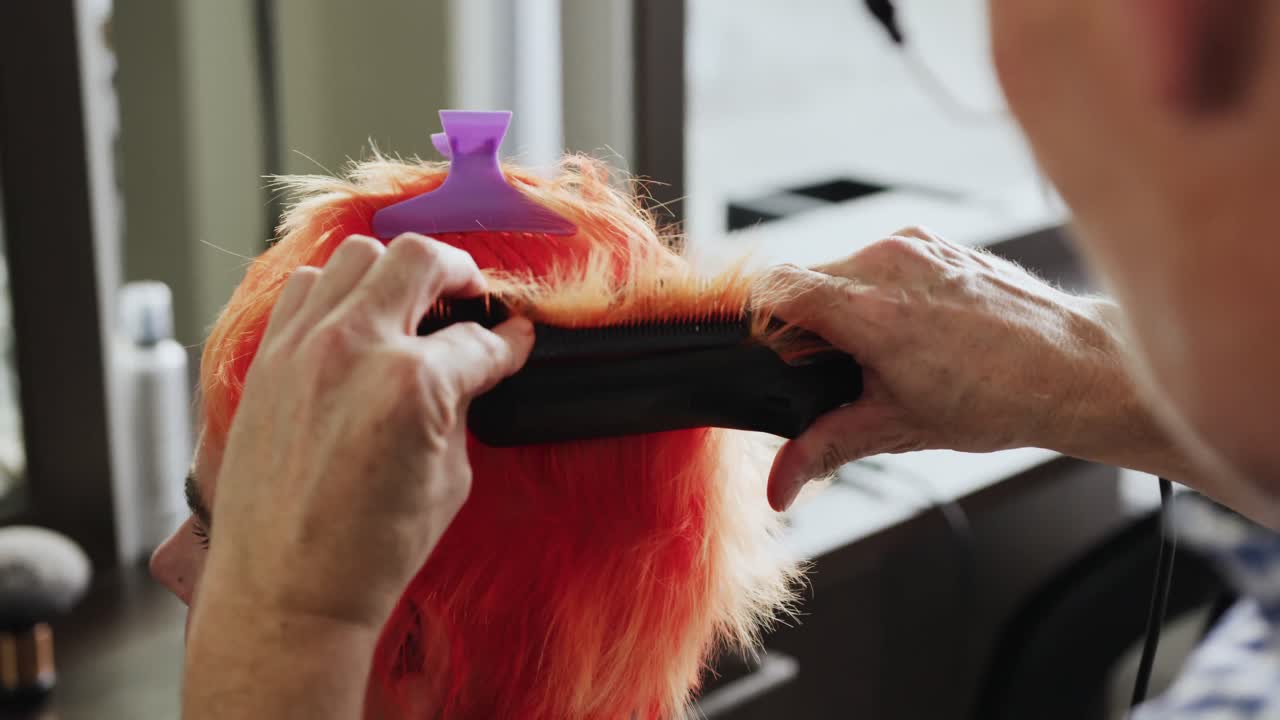 사이드 뷰 여성이 헤어 드라이어에 의해 머리를 곧게하고 있습니다.