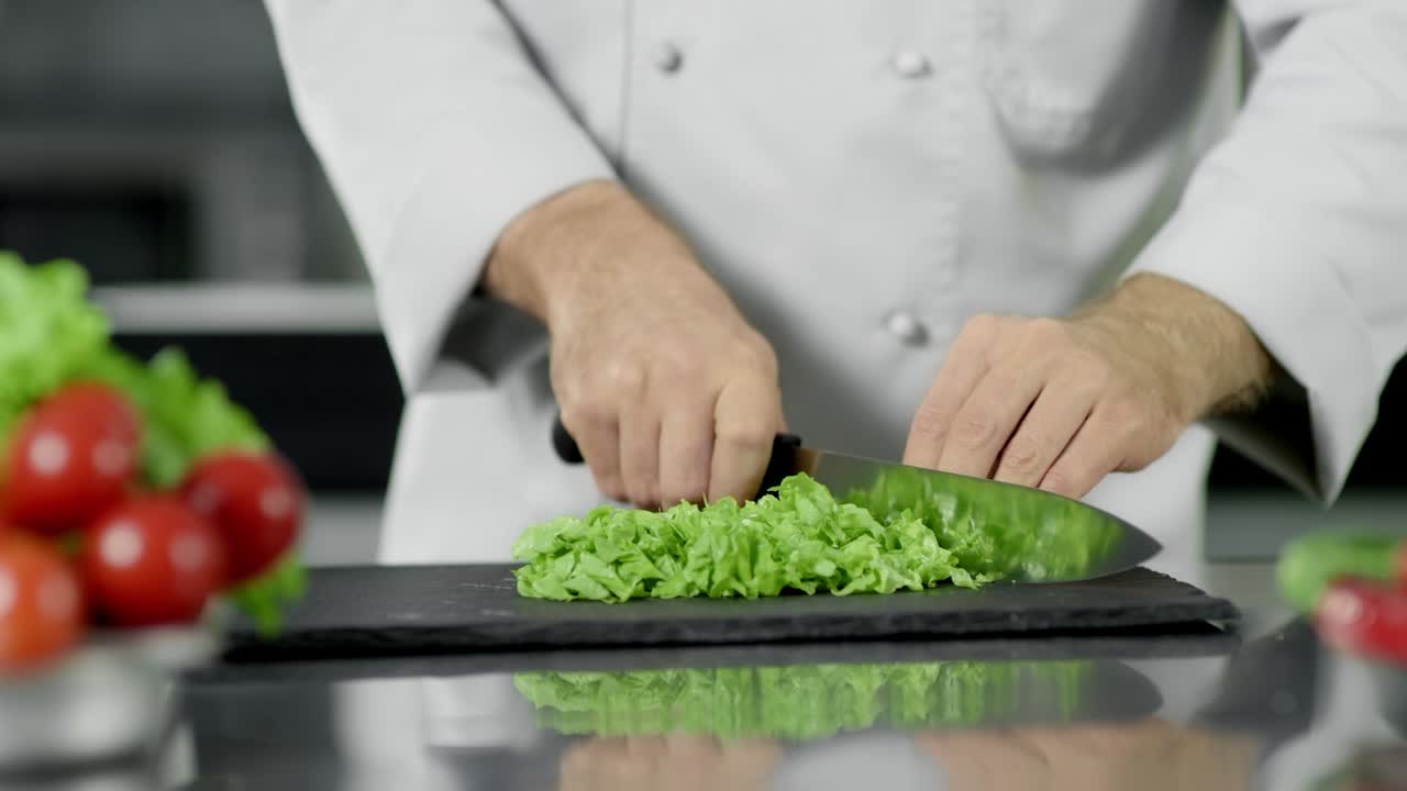 Mani dello chef che tagliano il cibo in cucina. Primo piano delle mani dello chef che tagliano l'insalata con un coltello.