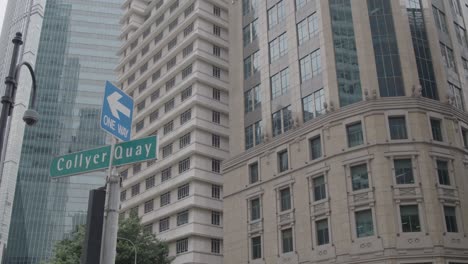 wide shot: camera pans from left to right in singapore, capturing a street sign in the foreground and skyscrapers in the background on a sunny day