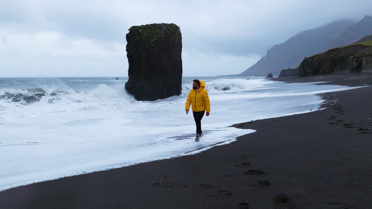 un hombre camina por la costa de la playa de laekjavik con olas espumosas en islandia