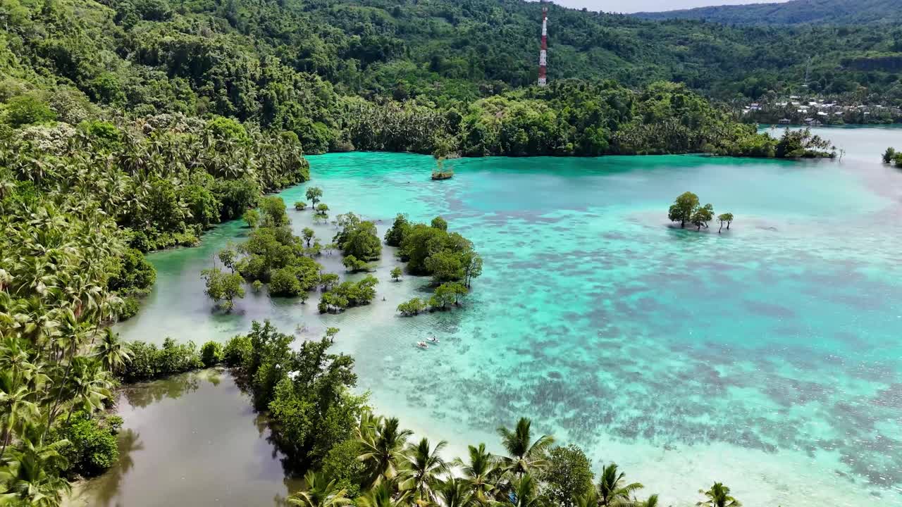 4K drone flying towards people paddle boarding off the coast of a tropical island in the Banggai Islands in Sulawesi, Indonesia. The island is covered in palm trees with white sand and blue ocean