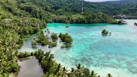 4k drone flying towards people paddle boarding off the coast of a tropical island in the banggai islands in sulawesi, indonesia. the island is covered in palm trees with white sand and blue ocean