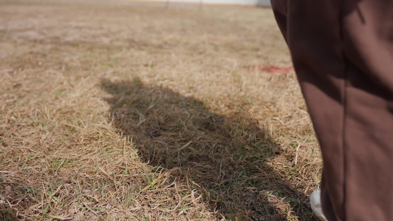 신발이 마른 풀이 무성한 지면을 누르는 모습, 마른 초원 표면과 함께 신발을 가까이에서 보여주는 장면, 운동화 밑창 질감 그림자와 자연스러운 발의 야외 위치를 클로즈업 시점으로 포착