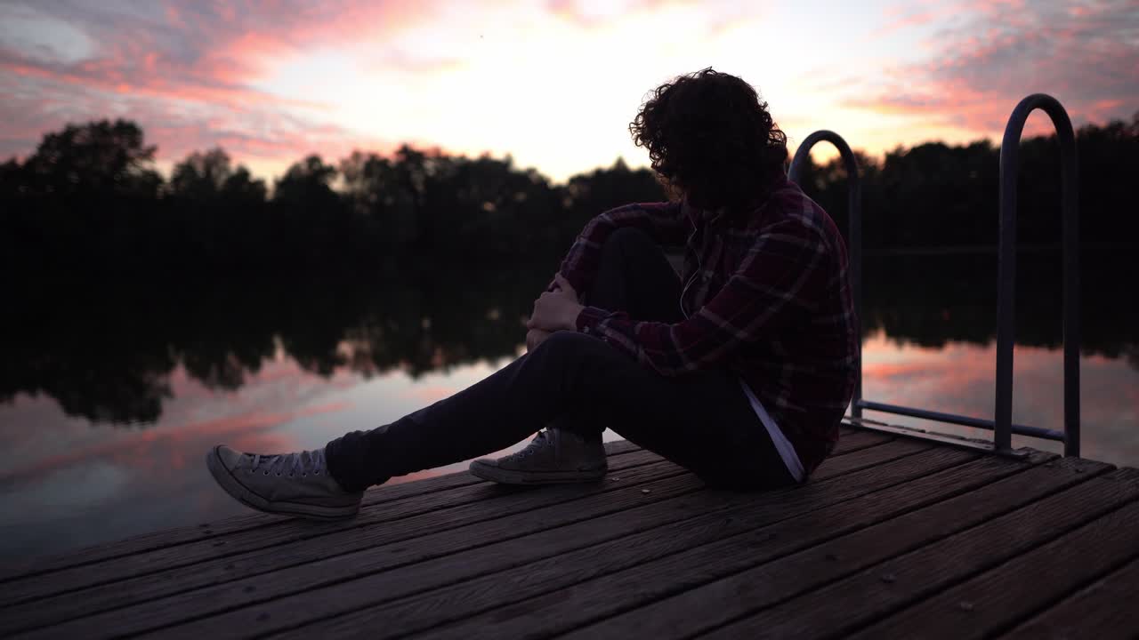 joven deprimido sentado y reflexionando sobre la vida con vistas al lago al atardecer