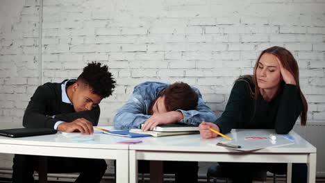 young students are bored during the lecture time while one of them is sleeping sitting at the table