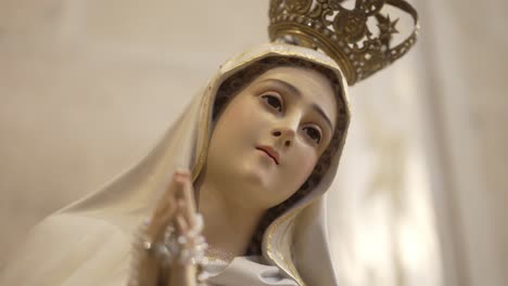 close-up of a statue of the virgin mary with a golden crown, hands clasped in prayer, in a serene expression