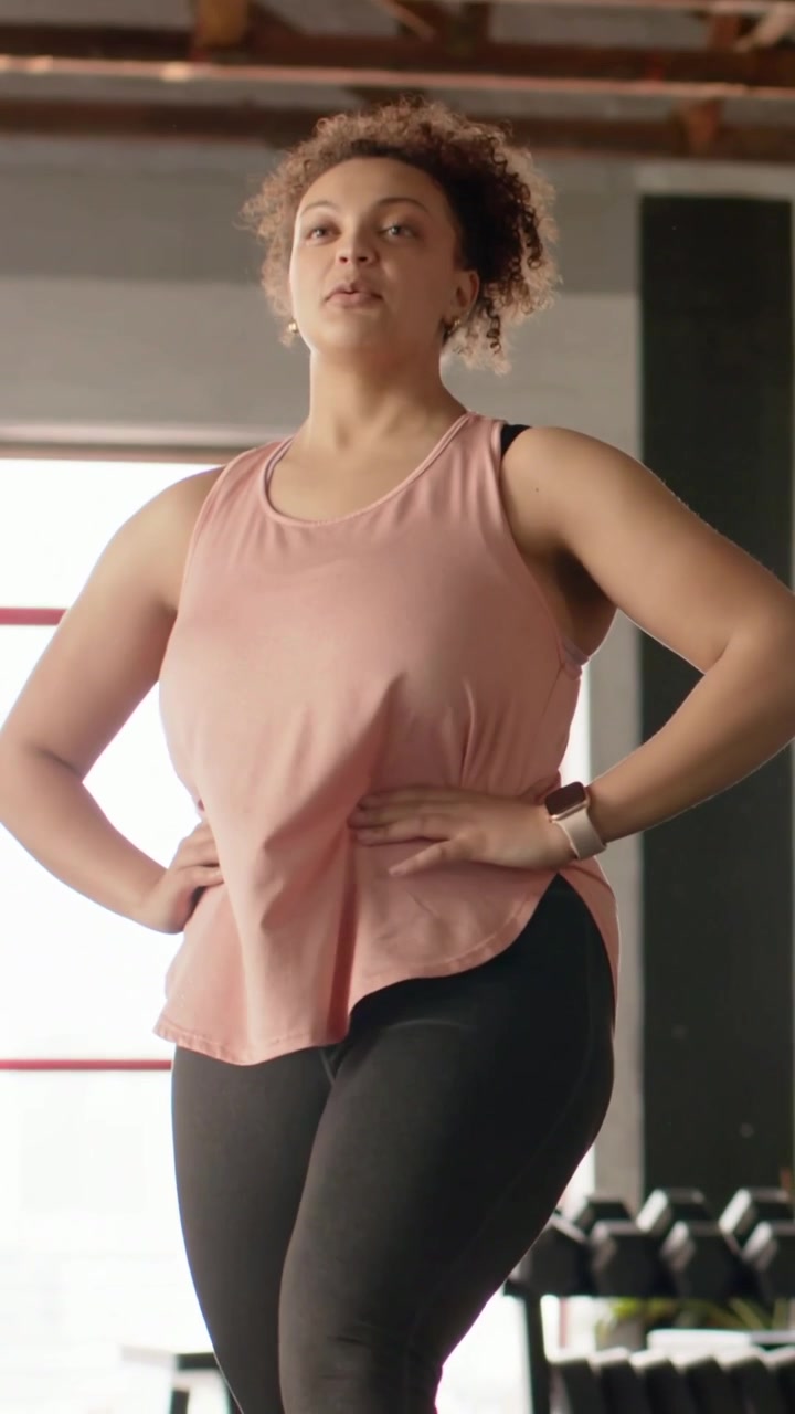 Donna che prende fiato e solleva il ginocchio in palestra, controllando lo smartwatch e preparandosi per l'allenamento.