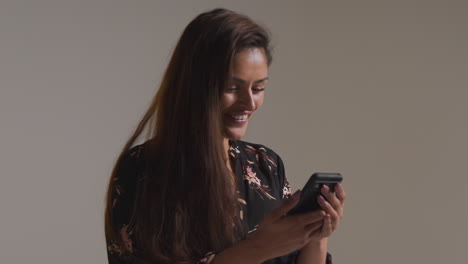 fotografía de estudio de una mujer sonriente con teléfono móvil recibiendo buenas noticias contra un fondo gris 1