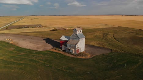 drone backward moving shot taken of a grainery called alberta pacific in alberta, canada for storing wheat harvested during autumn season with path connecting the grainery to a nearby town