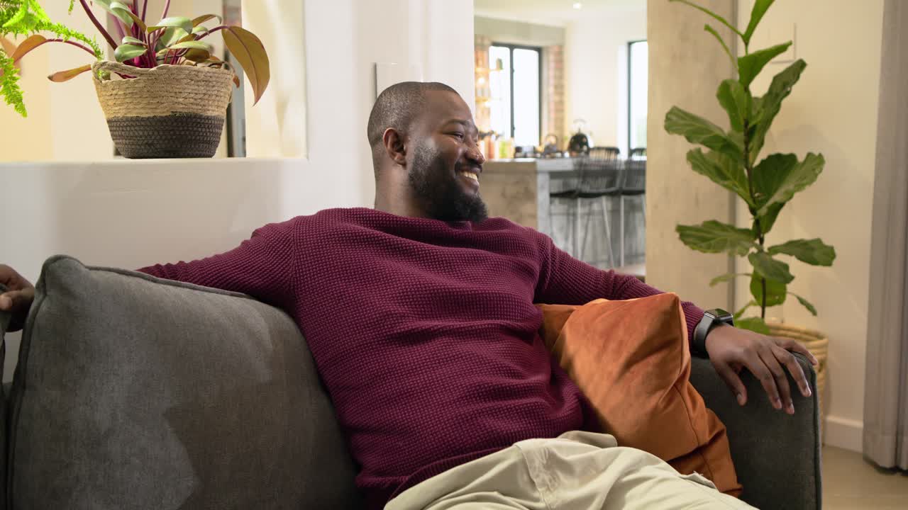 Noticing sideways movement, African American man leaning back on sofa, swiveling torso and smiling