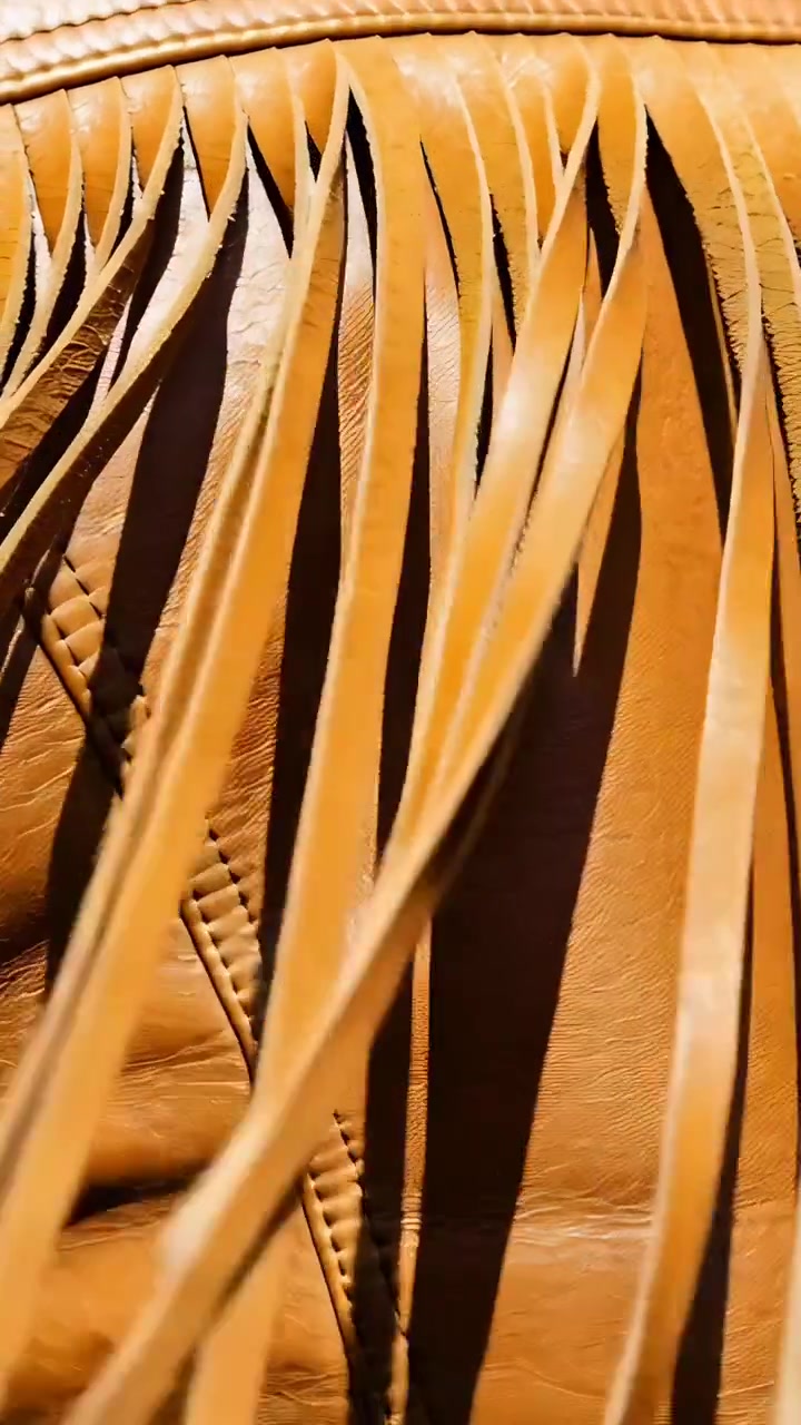 Video verticale: Telecamera in panoramica che sposta frange di pelle color cuoio su un pannello cucito, ombre che si spostano.