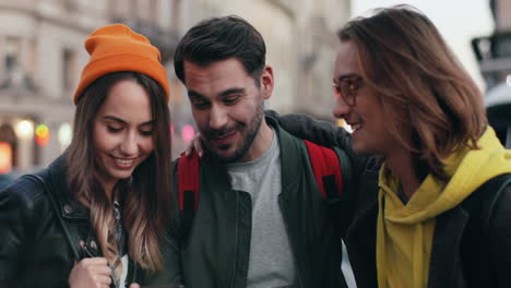 una joven pareja caucásica parada en la calle con un smartphone en las manos, luego aparece su amigo y le muestran algo gracioso