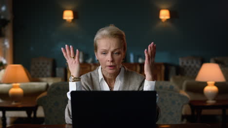 annoyed old woman having video call on laptop computer in vintage cabinet