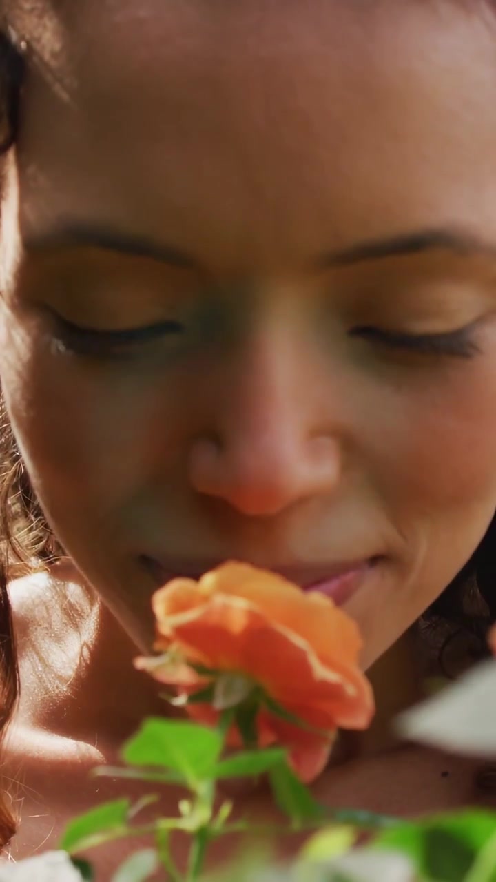 Video verticale: Donna che tiene una rosa arancione e la porta al naso, tecnologia HUD che appare e scansiona il viso.