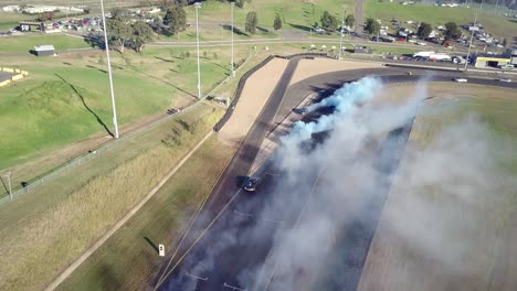 cars racing on asphalt race track with lots of smoke from burning tires - aerial shot