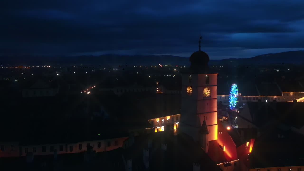 Aerial drone view of The Big Square in Sibiu at night, Romania. Old city centre decorated for Christmas. Ferris wheel, skating rink, bell tower, people