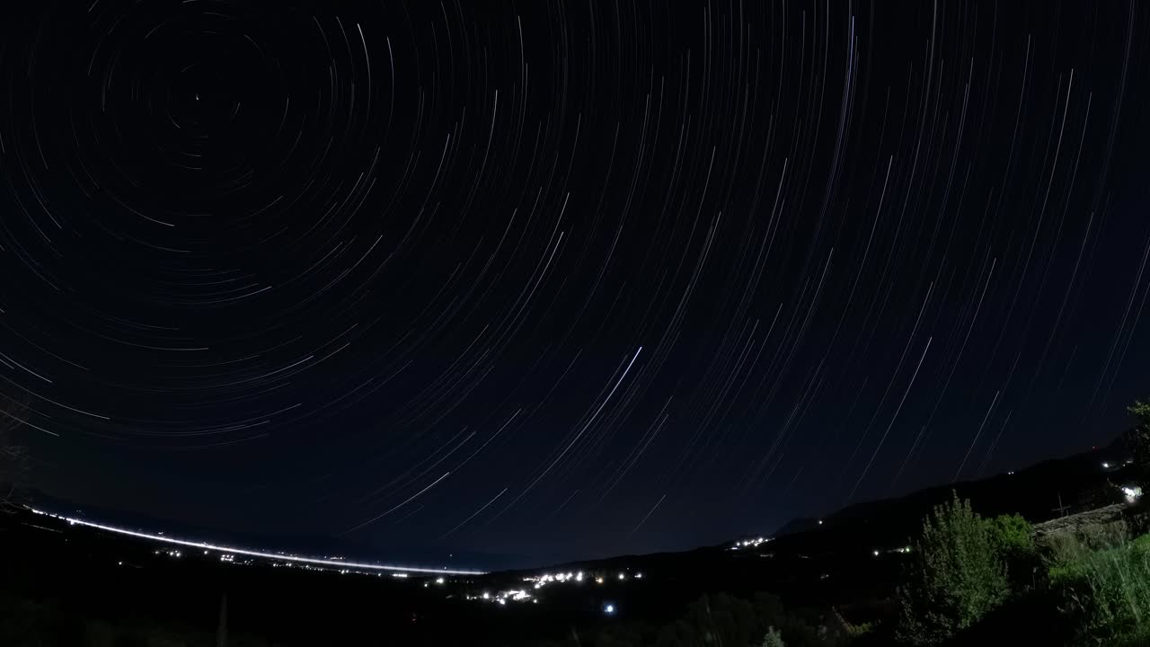 Long Exposure Star Trails Time Lapse Spinning Over Night City Lights and Mountain Landscape Astronomy Cosmos