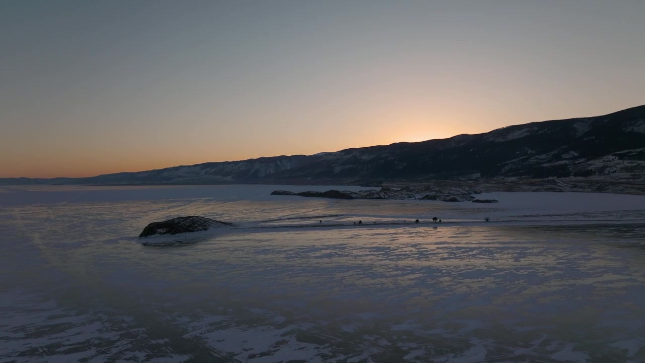 Luftoptagelser af en frossen Bajkalsø ved solnedgang, med snedækket is, klippeøer og bjergkam i horisonten, Sibirien, Rusland om vinteren.