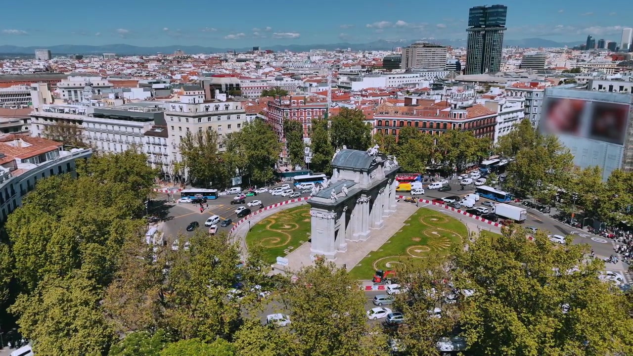 Ripresa aerea della rotonda di Puerta de Alcalá con lo skyline di Madrid e strade trafficate.
