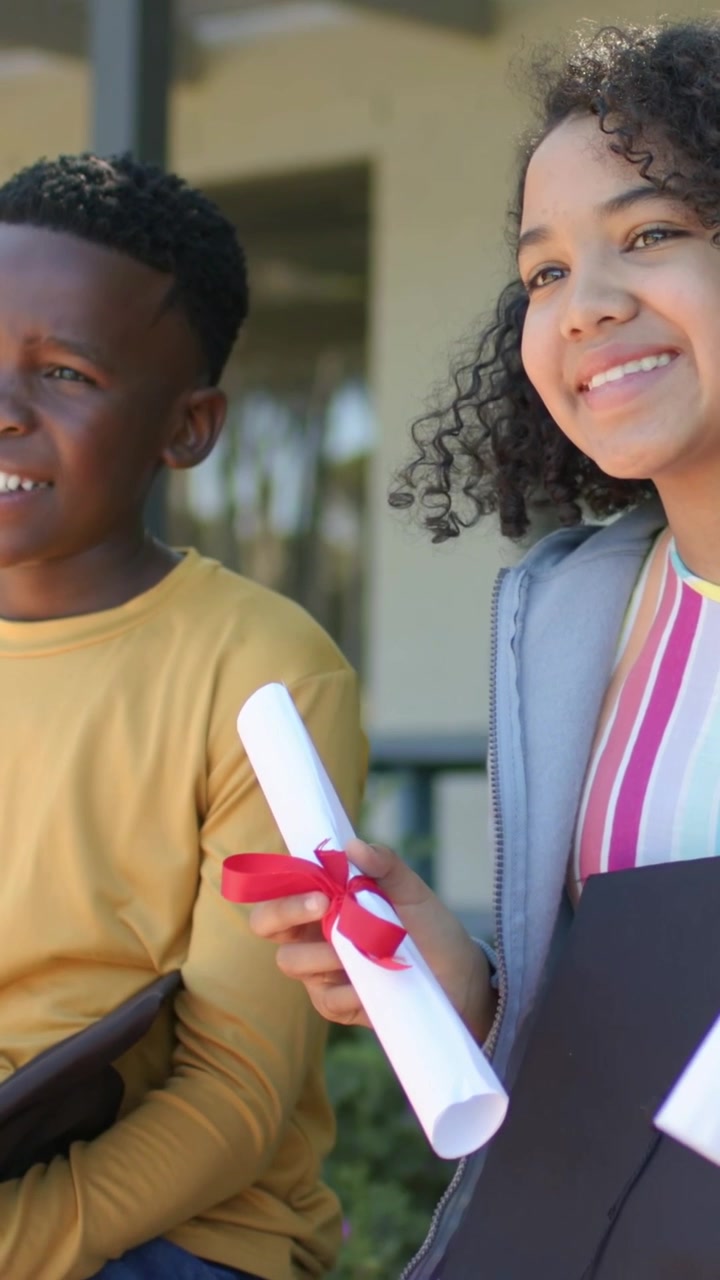 Vertical video: Sitting duo wearing yellow on porch for grad as hand showing red-ribbon diploma