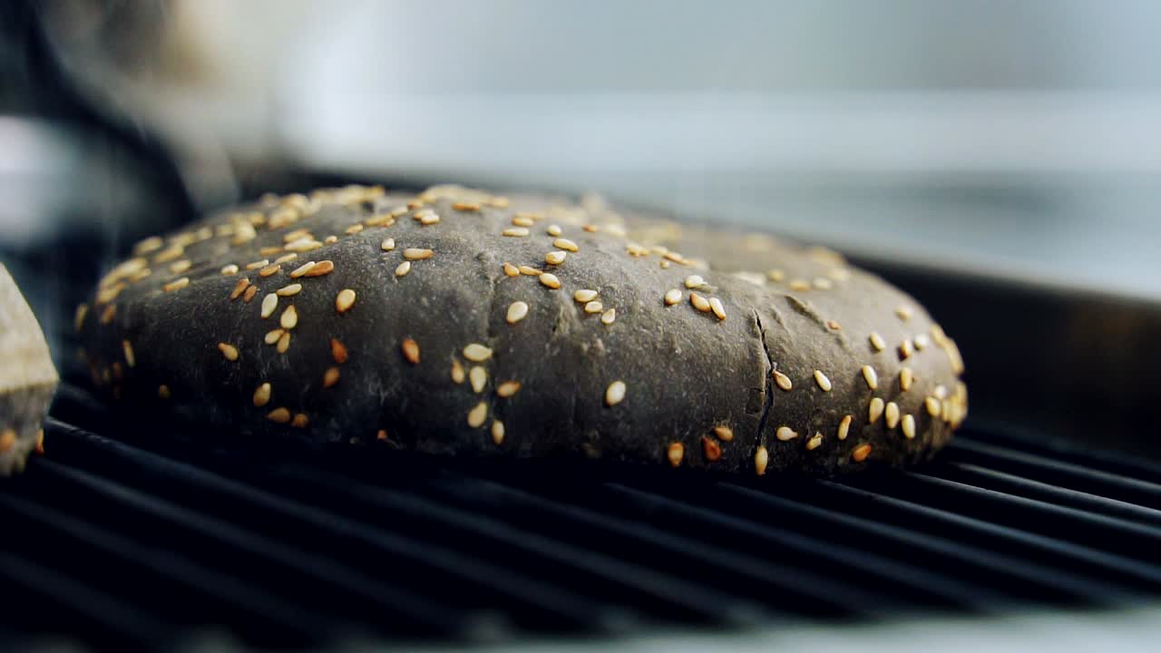 Black bun on hot grill. Brown bread for hamburger with sesame seeds is frying. Grilling bun for burger. Cooking delicious fast food. Close-up